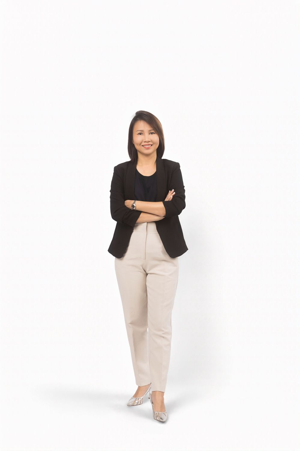 Professional in a black blazer and beige pants stands confidently against white background with arms crossed.