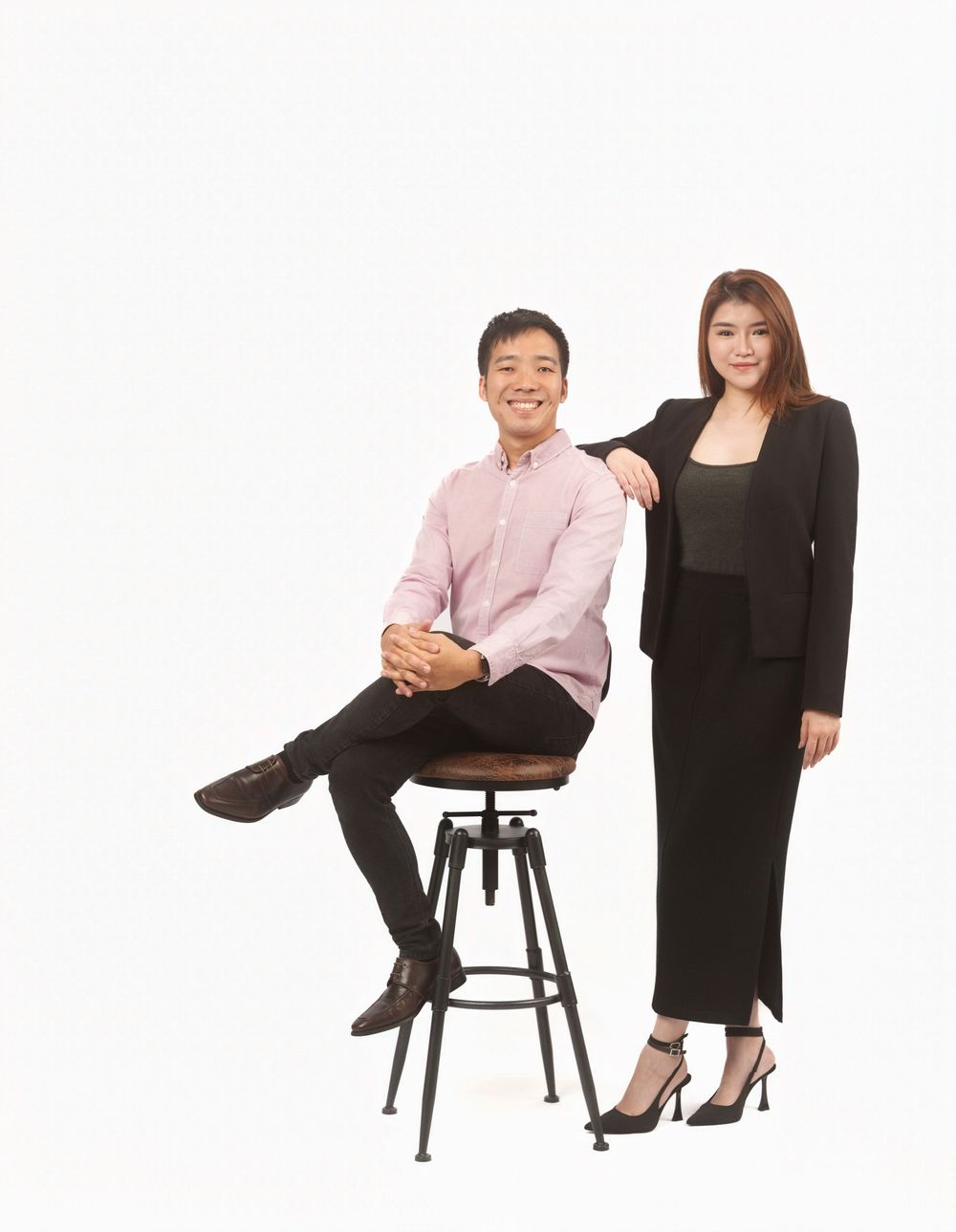 A series of three identical images showing two people in formal attire sitting and posing on dark stools against a white backdrop.