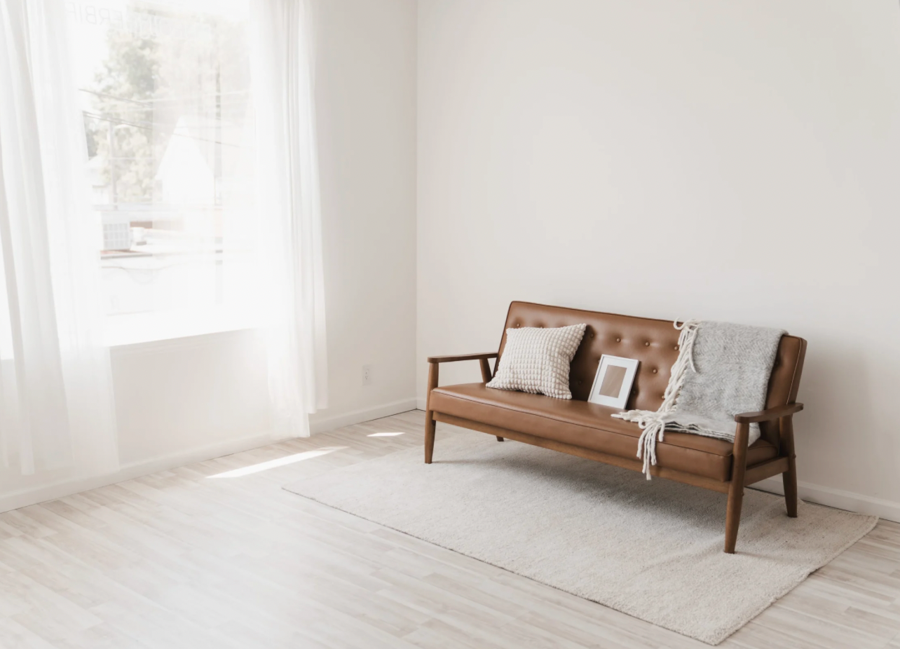 Minimalist living room featuring a brown leather mid-century modern sofa against white walls.