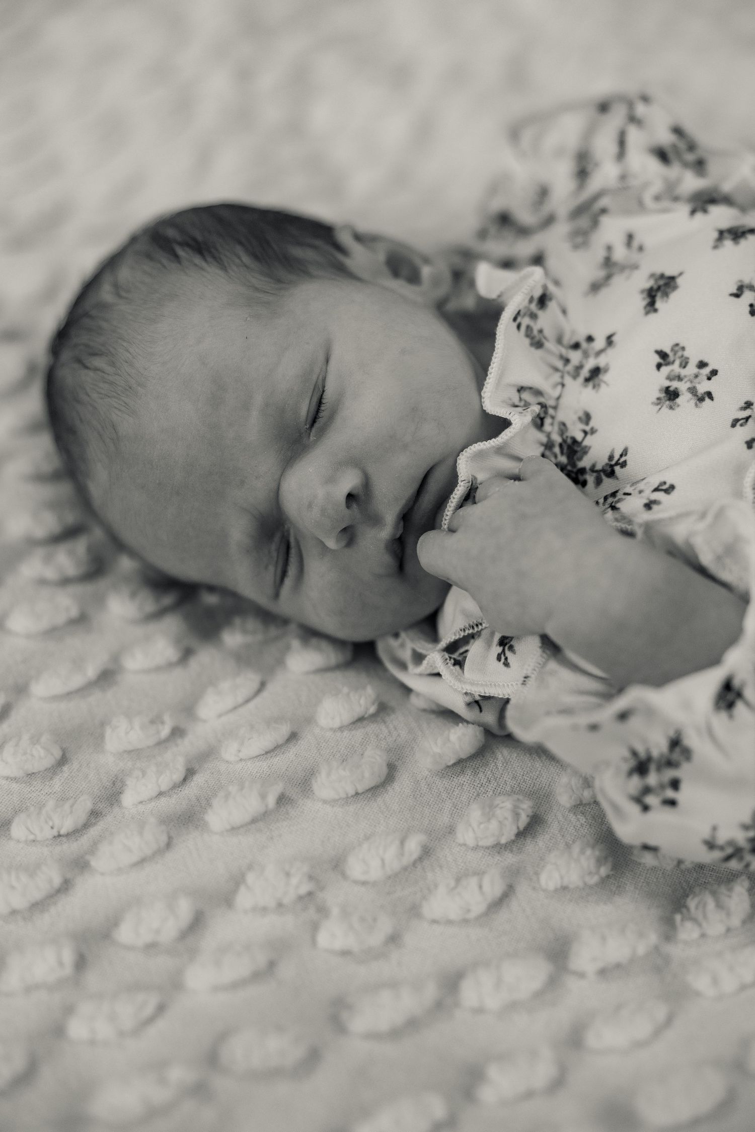 Sleeping newborn baby in soft pink clothing lying on white bedding.