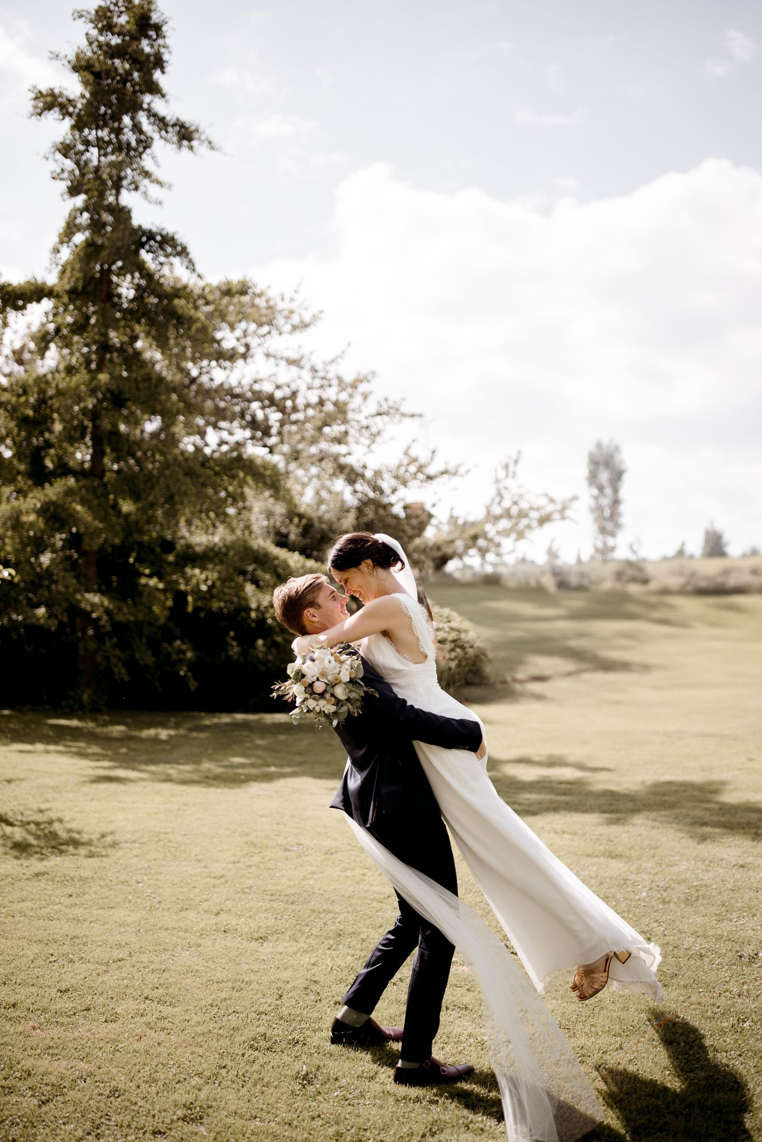 Un couple de mariés partage un moment romantique alors que le marié soulève sa mariée sur une colline ensoleillée.