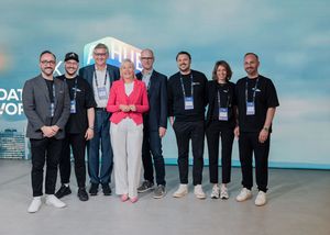 A group of conference attendees in business casual attire pose together for a photo against a blue backdrop.