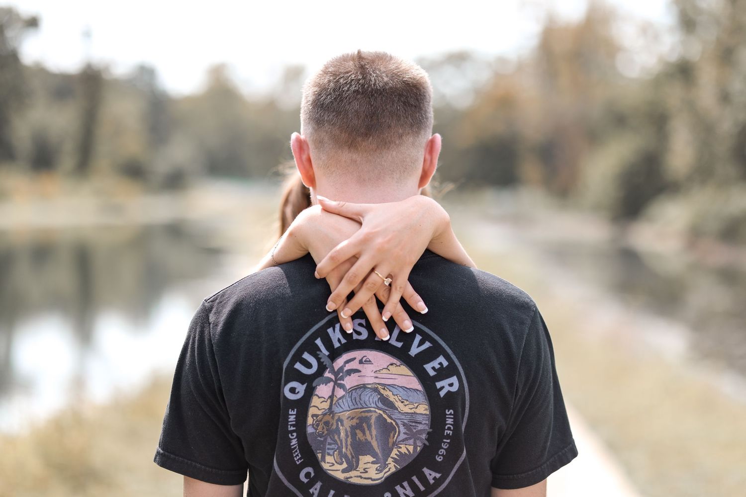 Back view showing arms wrapped around neck with lake and nature in background.