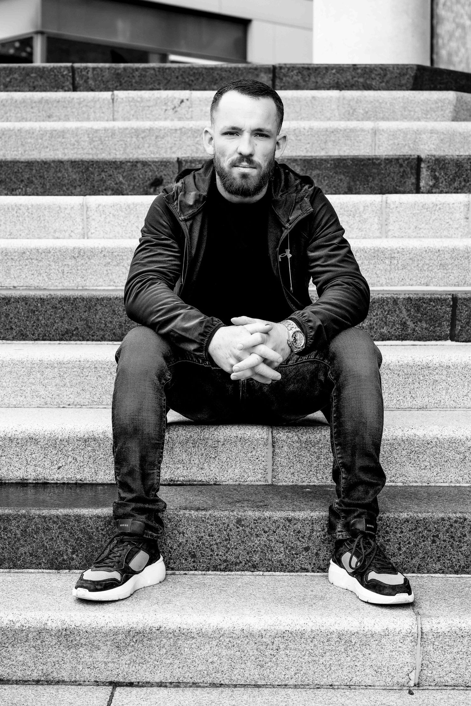 Person in leather jacket sitting on concrete steps in black and white portrait.