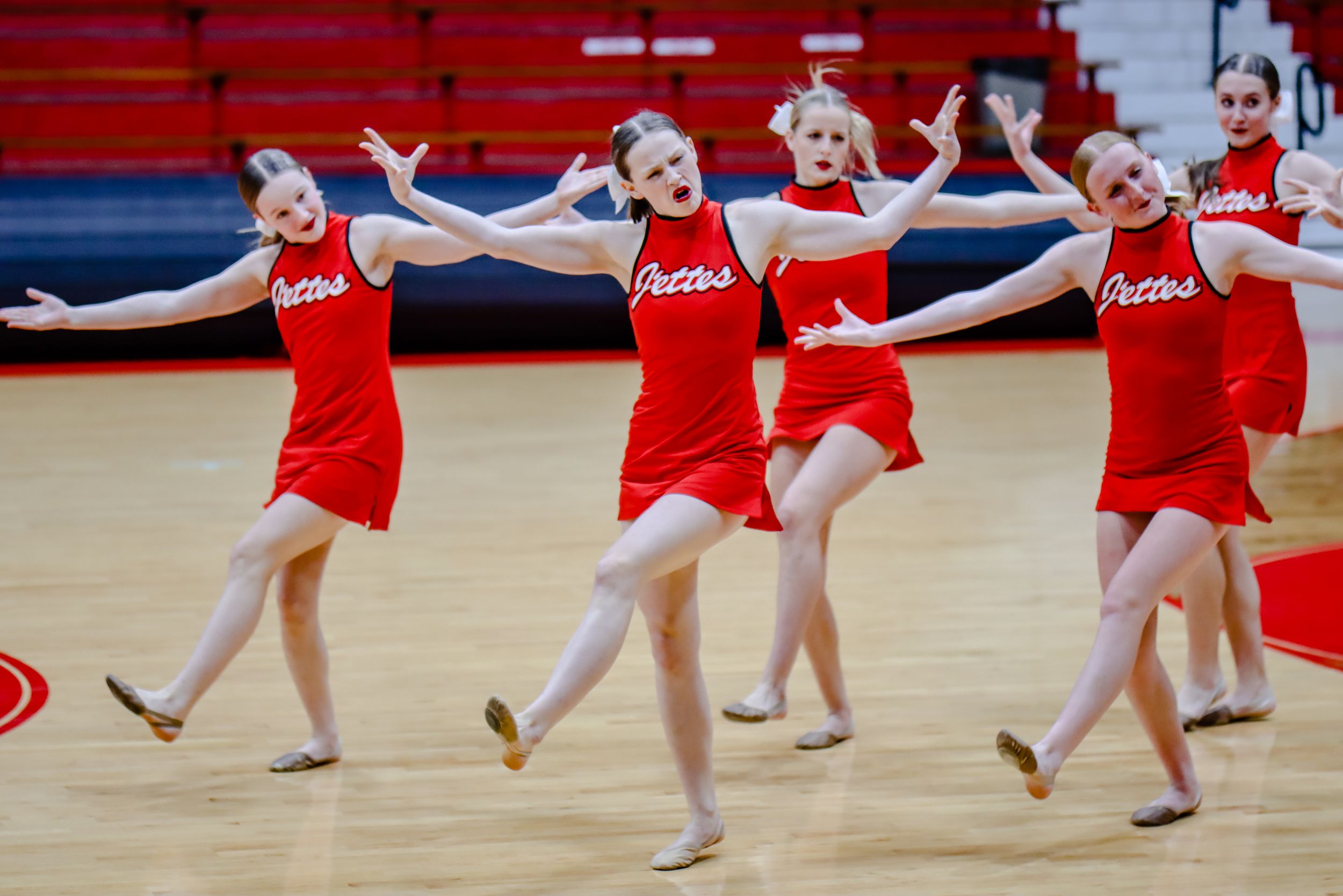 Dance team in red uniforms performing synchronized routine on gymnasium floor.