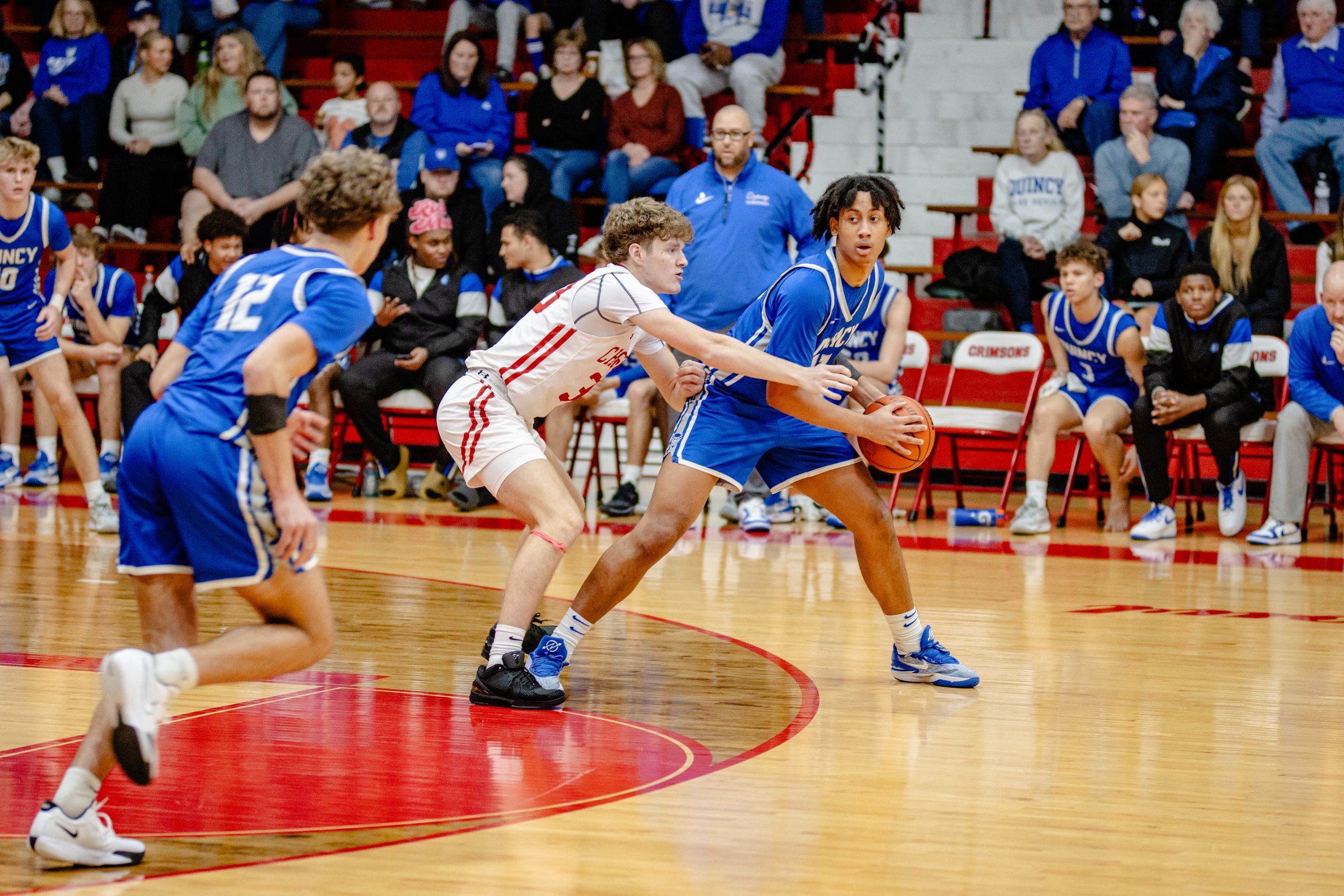 Basketball players diving for a loose ball during an intense game on a red court.