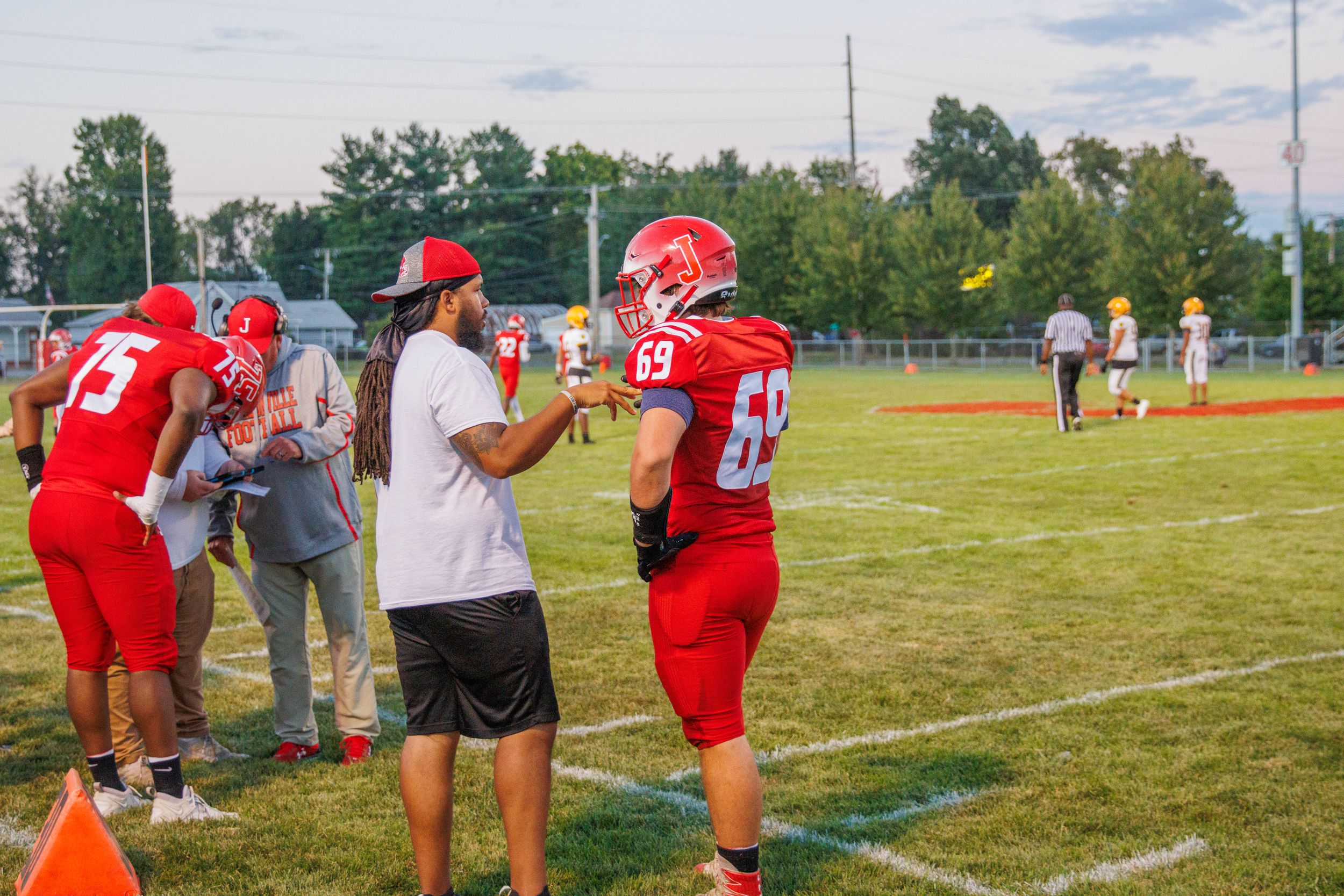 Youth football practice on a sunny field with players and coaches in red uniforms.
