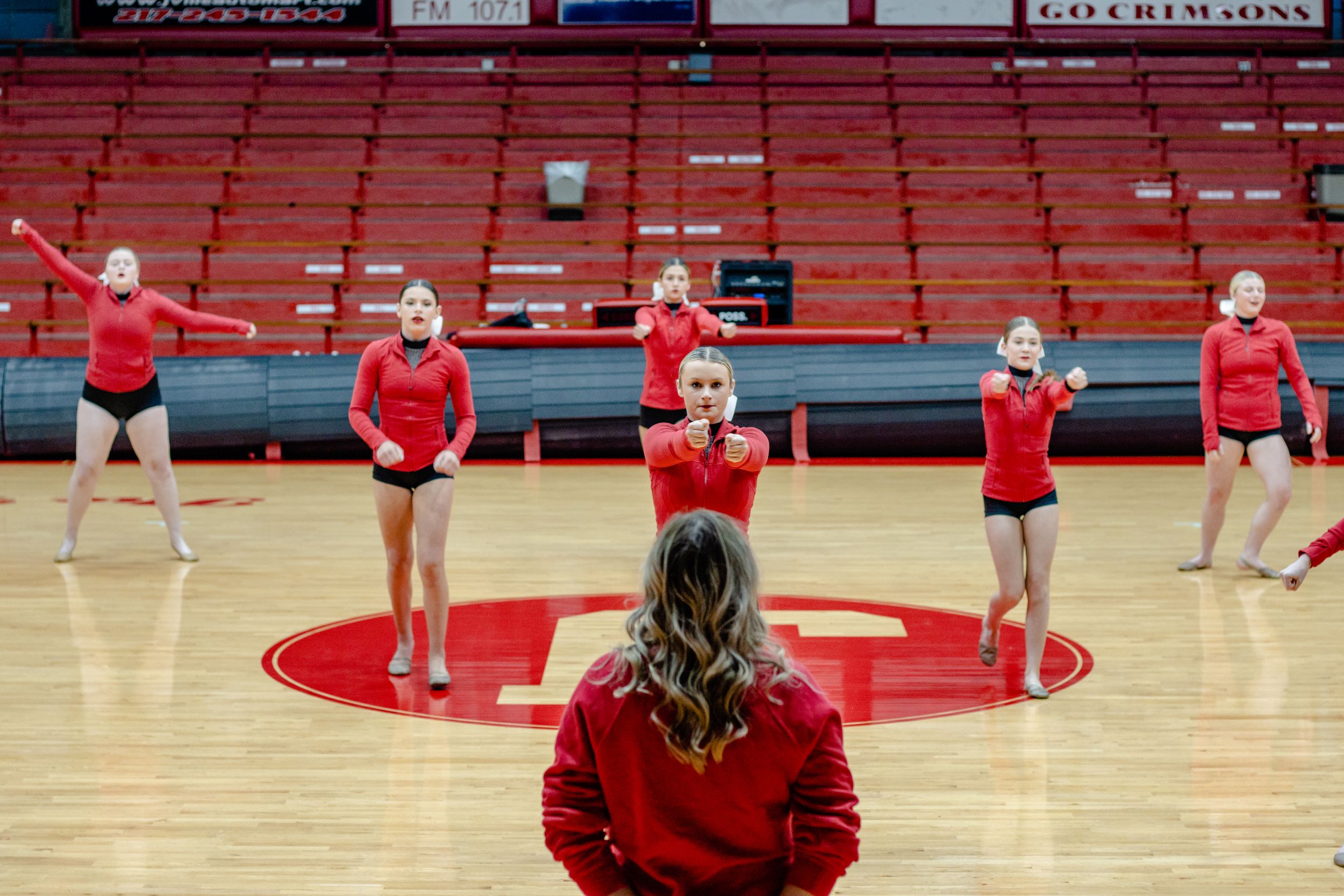 Performance group practicing choreography in red uniforms on indoor court.