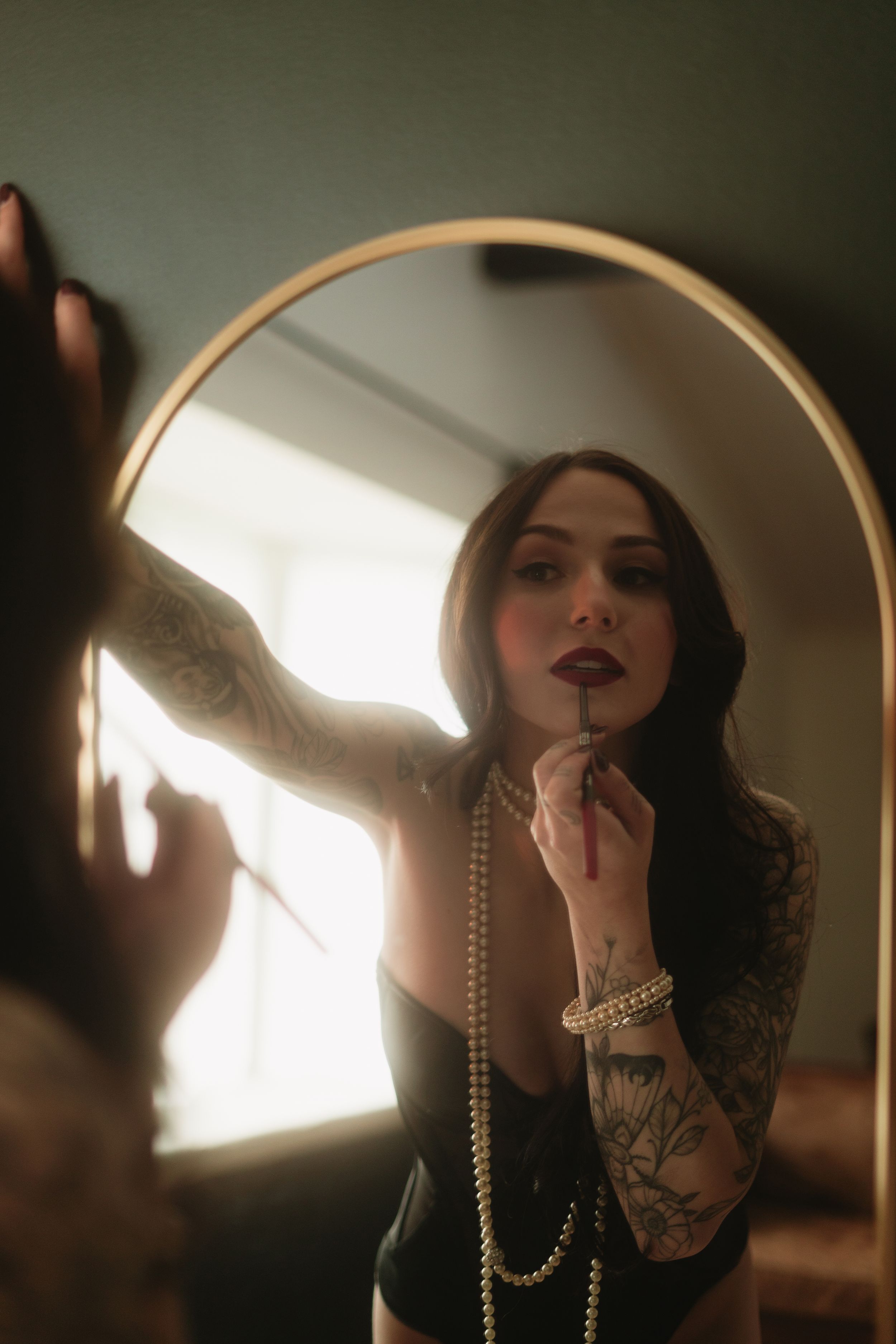 Vintage-inspired photograph with pearl necklace and rouge lipstick application reflected in round mirror in warm lighting.