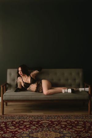Dark interior scene with vintage tufted gray couch on patterned red carpet against moody green wall.