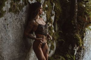Atmospheric portrait against a mossy rock wall in dark, moody lighting.