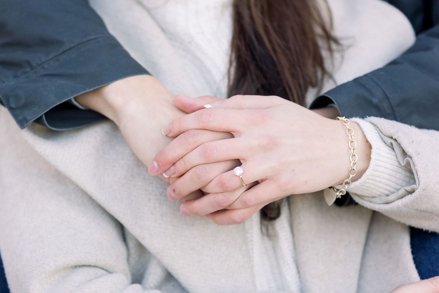 Close-up details of hands and jewelry against neutral clothing.