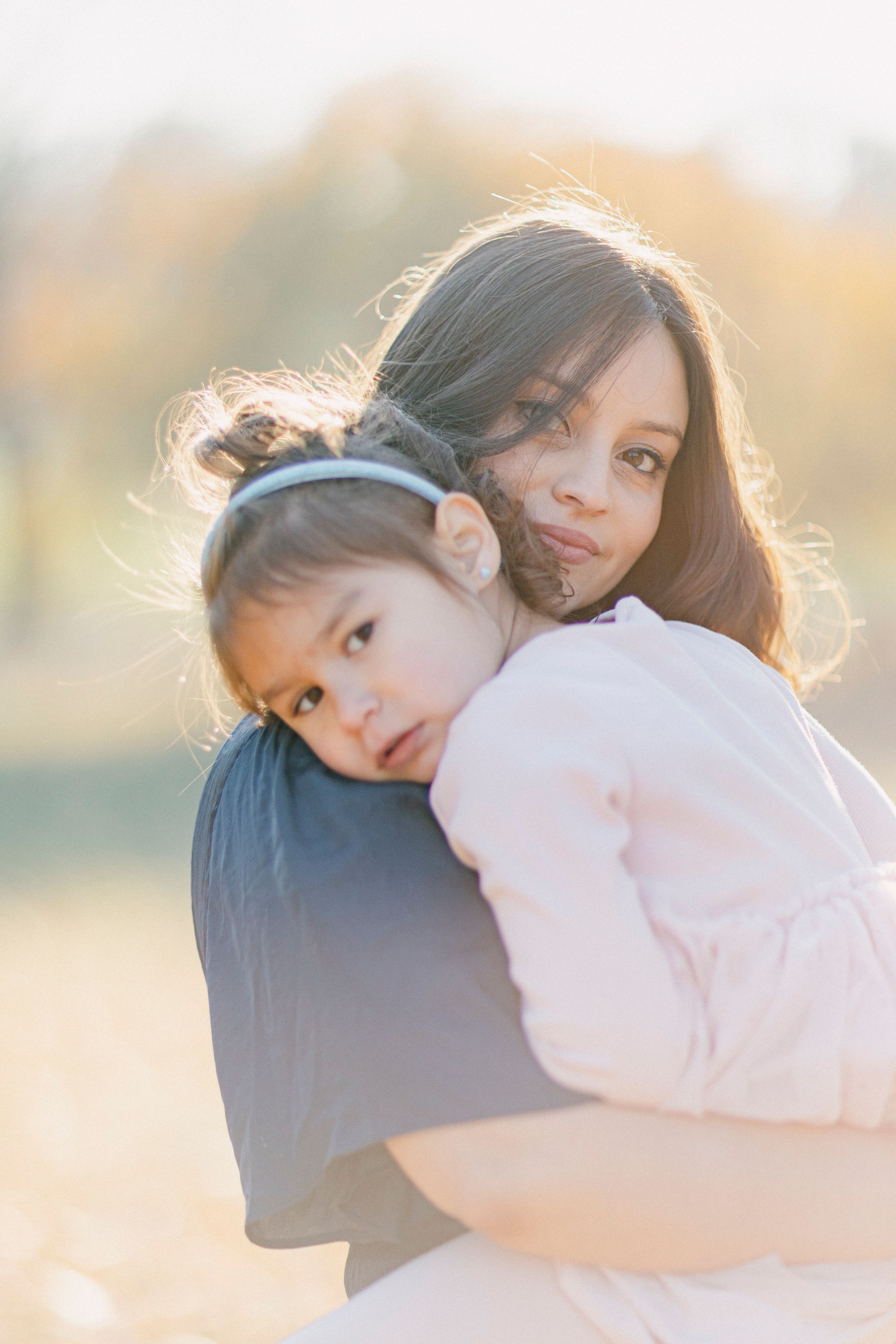 Parent and child share an intimate embrace during outdoor portrait session at sunset.