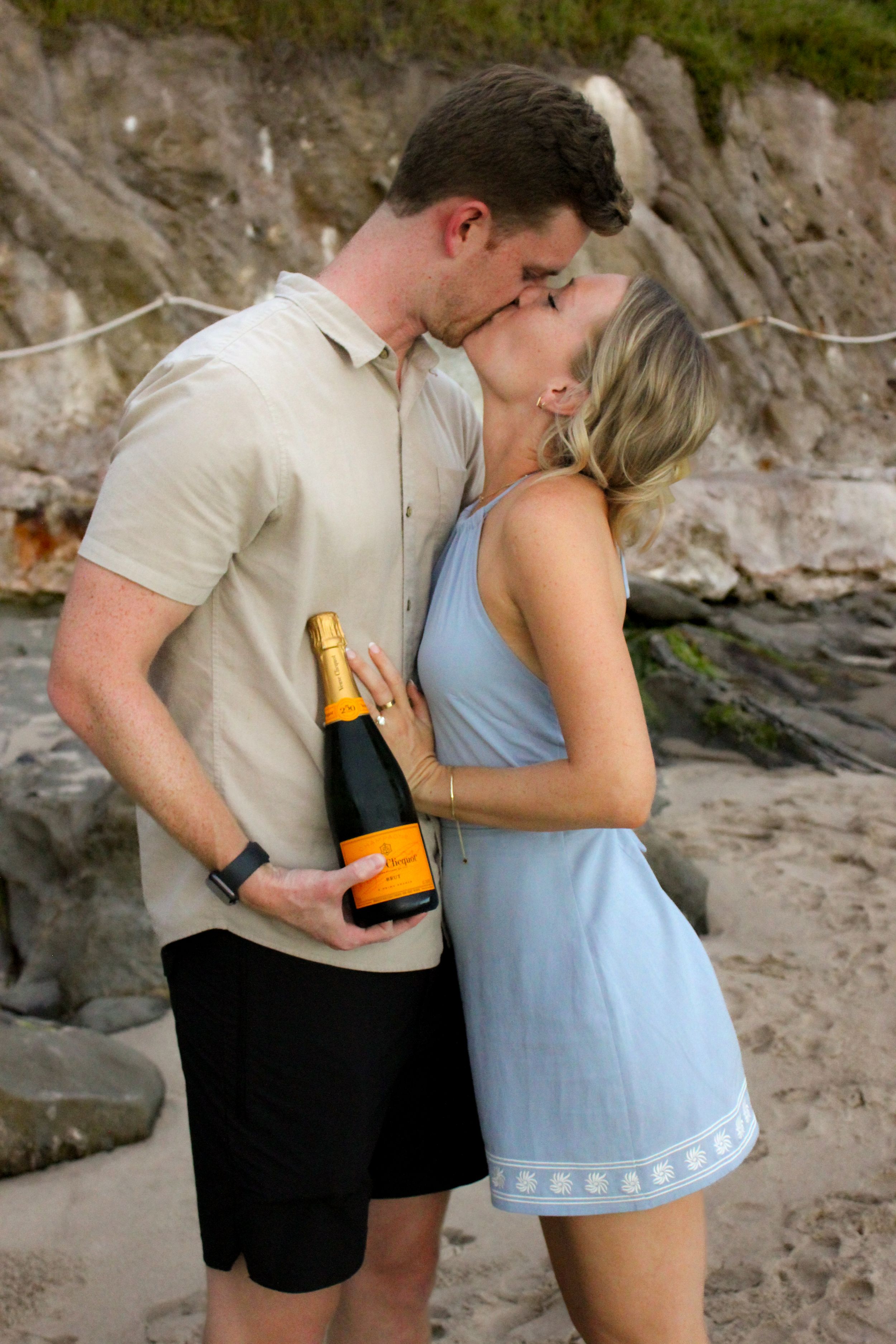 Veuve Clicquot Engagement Ring Photography Blue Dress Beach Couple embrace each other in a kiss