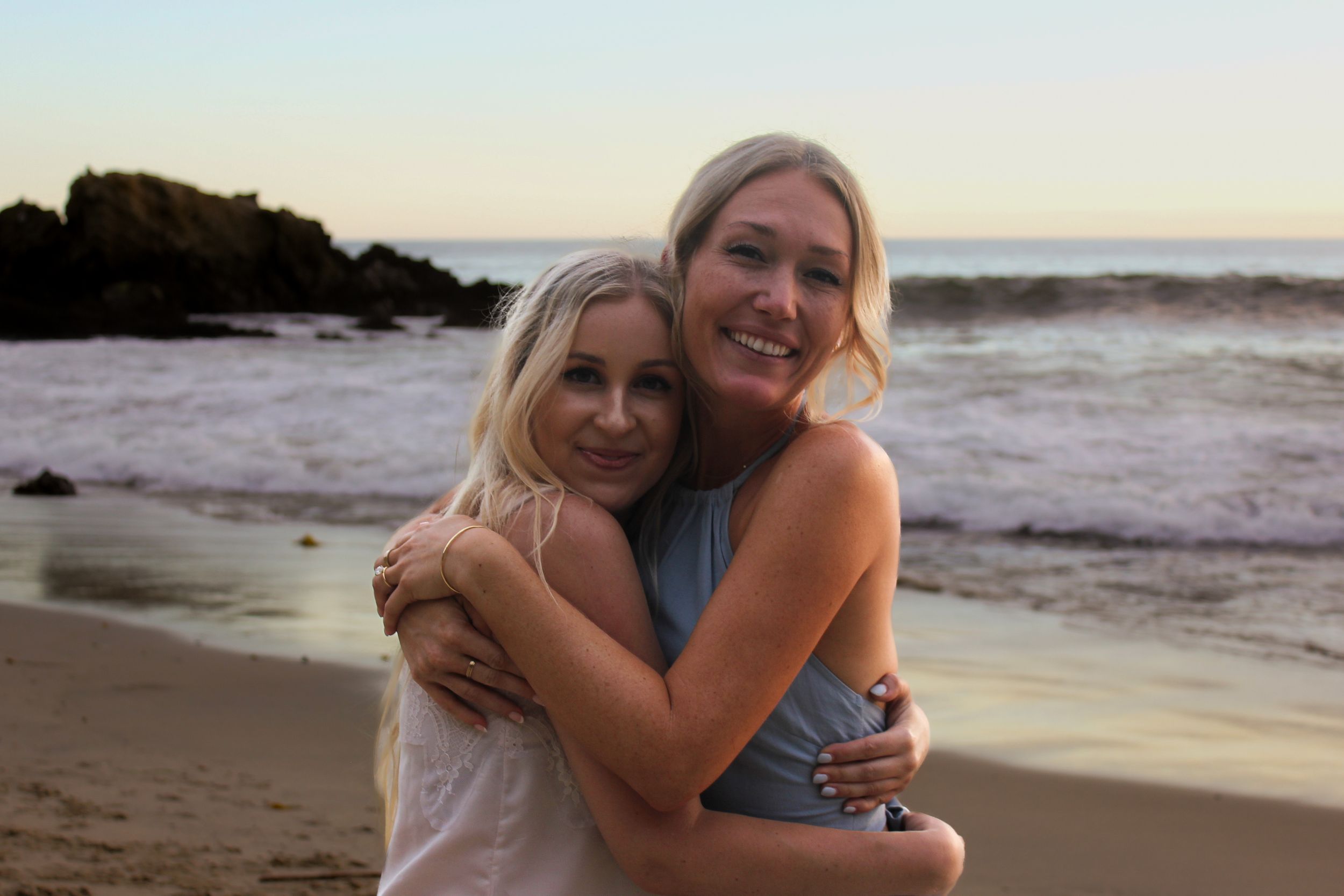 Photoshoot of two friends celebrating a recent engagement on a beach in Laguna Beach. waves crash upon the shore with a rocky shoreline.