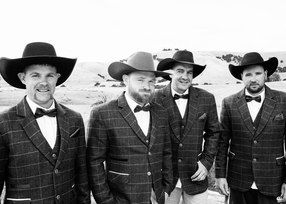 Black and white wedding photo of groom and his groomsmen in cowboy hats, bow ties and jackets.