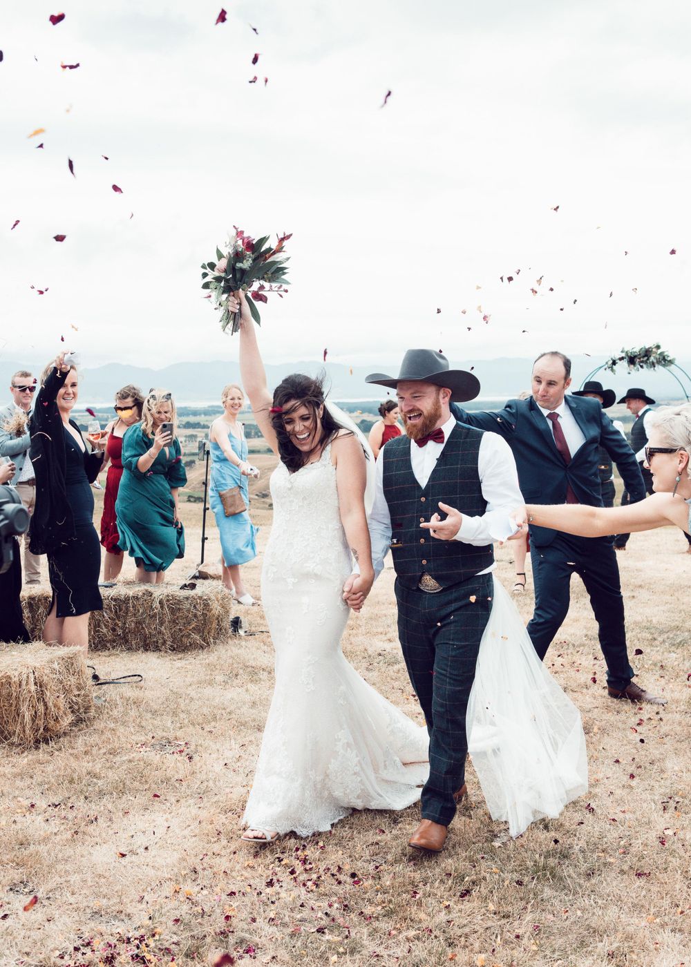 Wedding photo of couple walking down the aisle at an outdoor wedding bride holding bouquet up under confetti