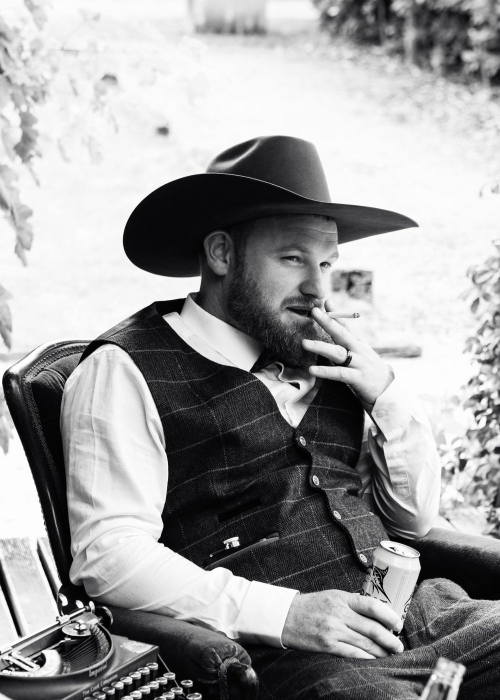Black and white wedding photo of groom in a cowboy hat smoking a cigarette.