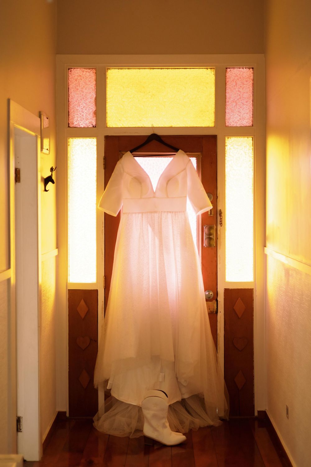 Wedding photo of wedding dress hanging against coloured glass.