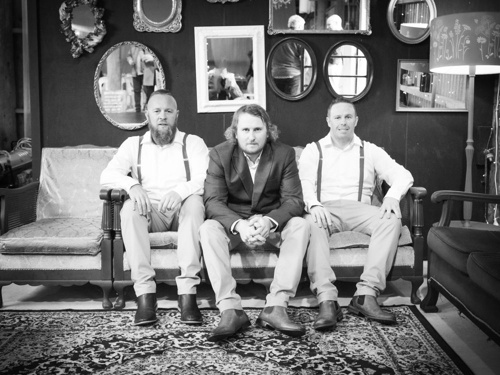 Wedding photo of groom and groomsmen sitting on a couch against a wall covered in mixed-sized mirrors.