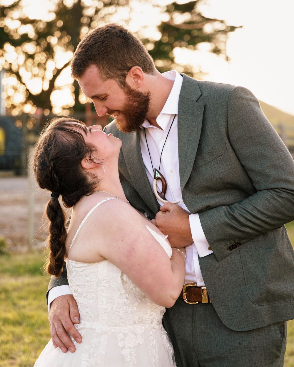 A tender moment between newlyweds embracing at sunset, with the bride in white and groom in gray suit.