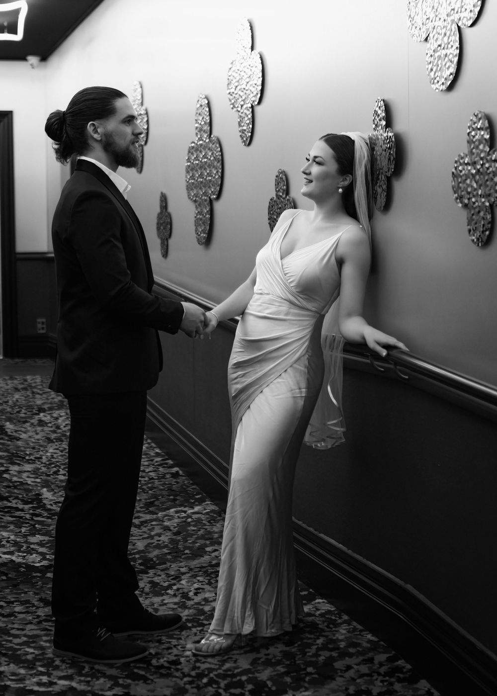 Black and white photo of a couple in formal attire holding hands in an elegant hallway.