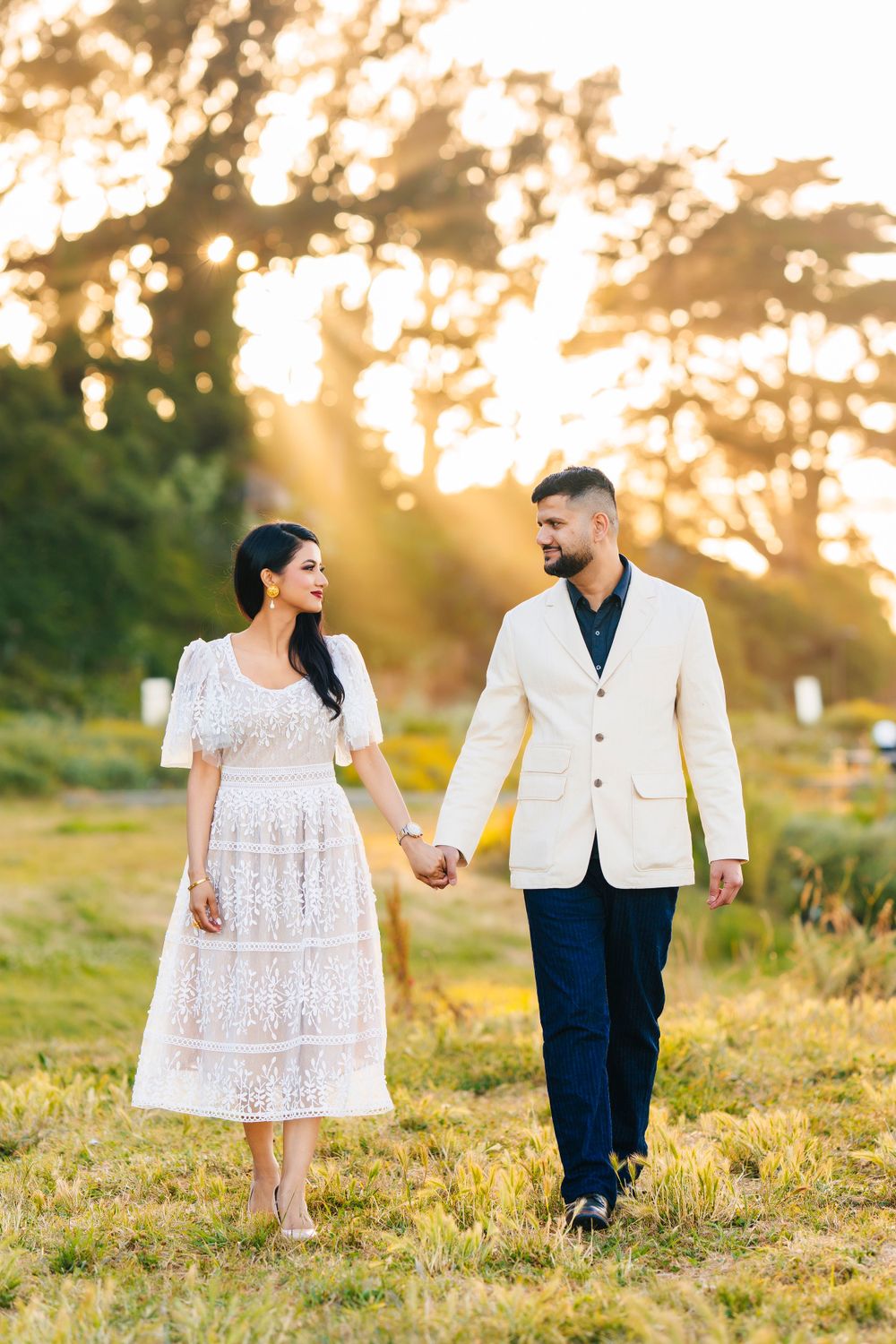 Elegant couple walking hand in hand through golden field during sunset portrait session.
