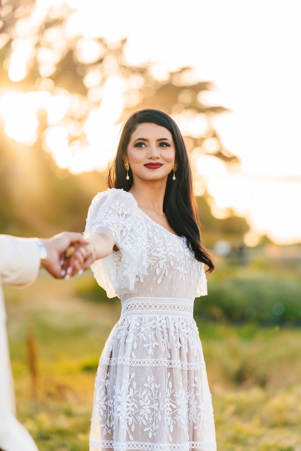 Woman in lace white dress holding hands during sunset outdoor photoshoot.