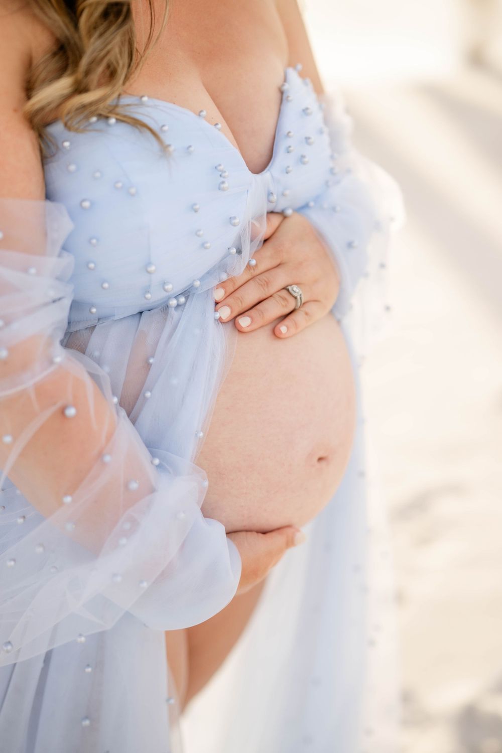 Detail shot of maternity gown with pearls and sheer fabric highlighting pregnancy.