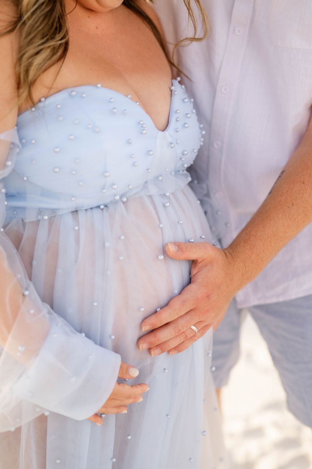 Close-up of light blue maternity dress with pearl details and sheer sleeves.