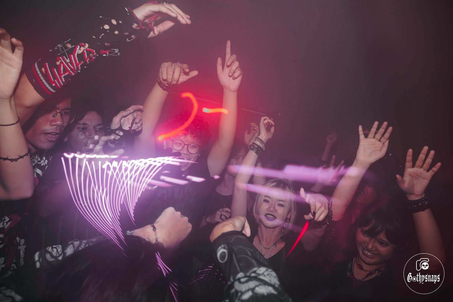 Three people enjoying a night out at a bar under red neon lighting while posing and making peace signs.