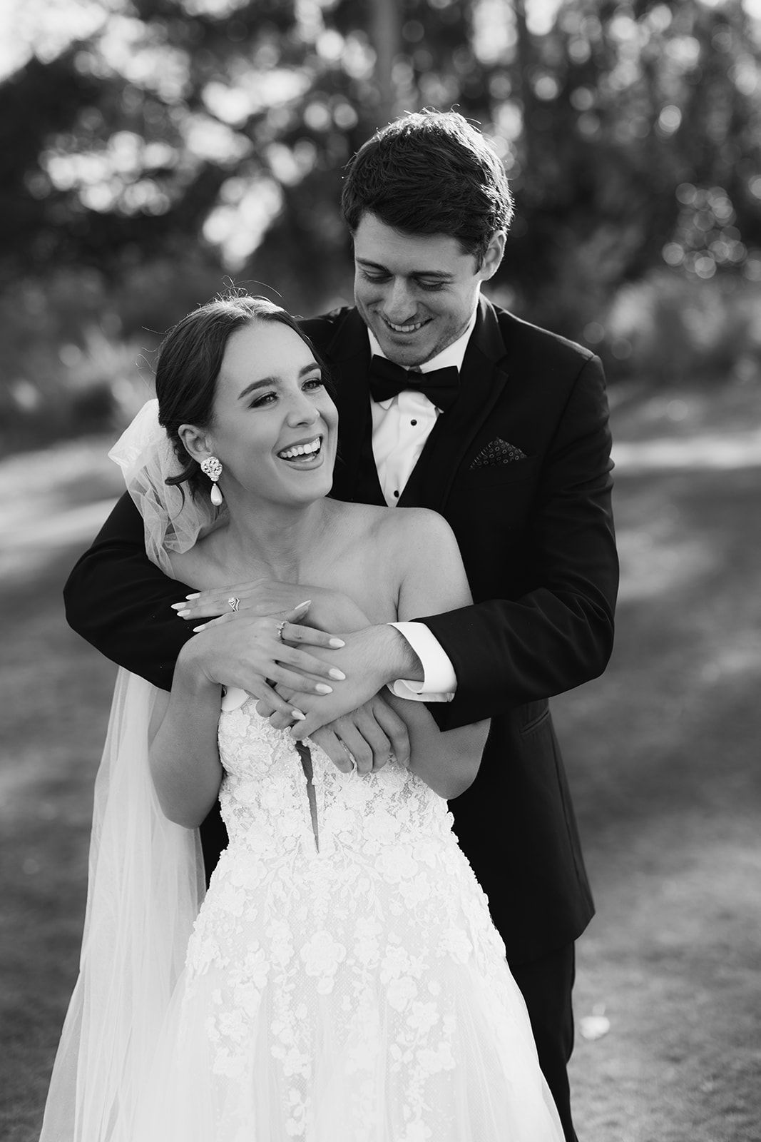 A loving black and white wedding photo showing a joyful couple embracing and laughing together outdoors.