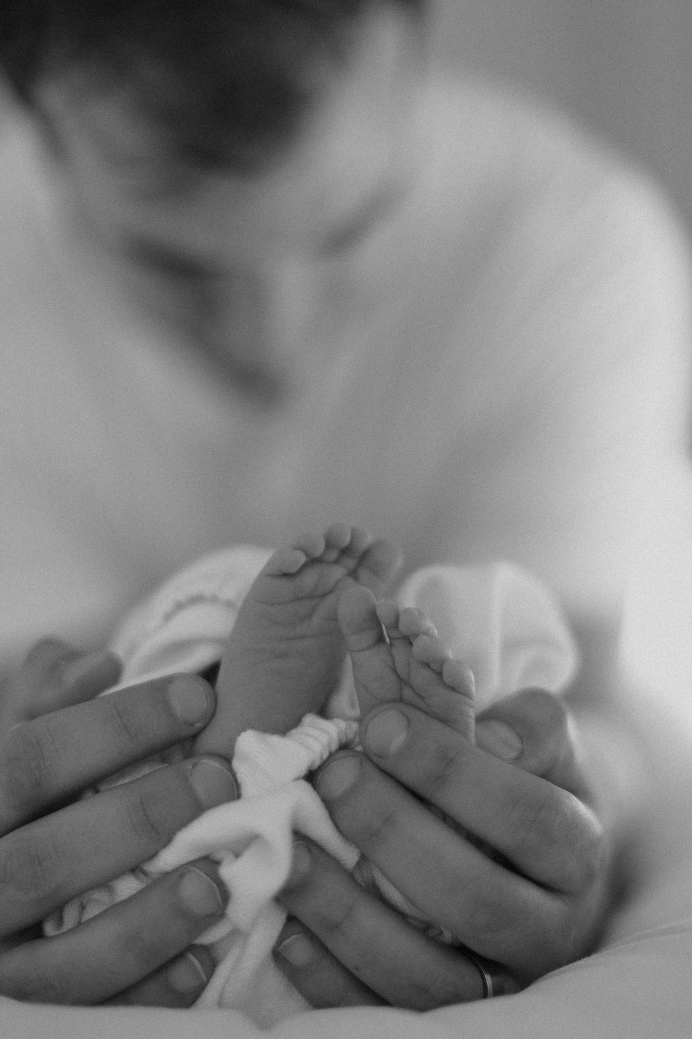 A close-up black and white photo of tiny baby feet being gently held in adult hands.