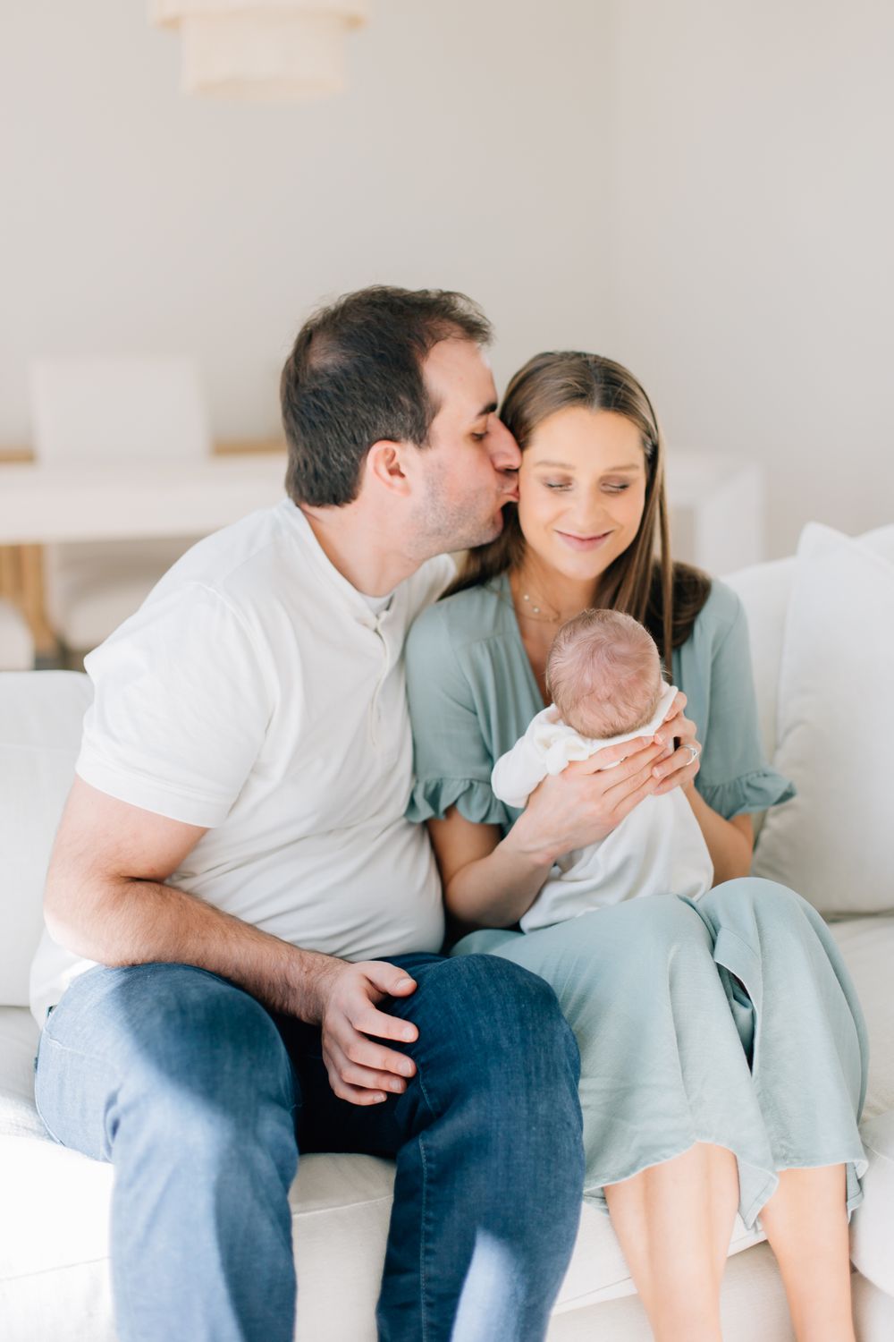 A tender family moment at home as parents share a sweet interaction while holding their newborn baby.