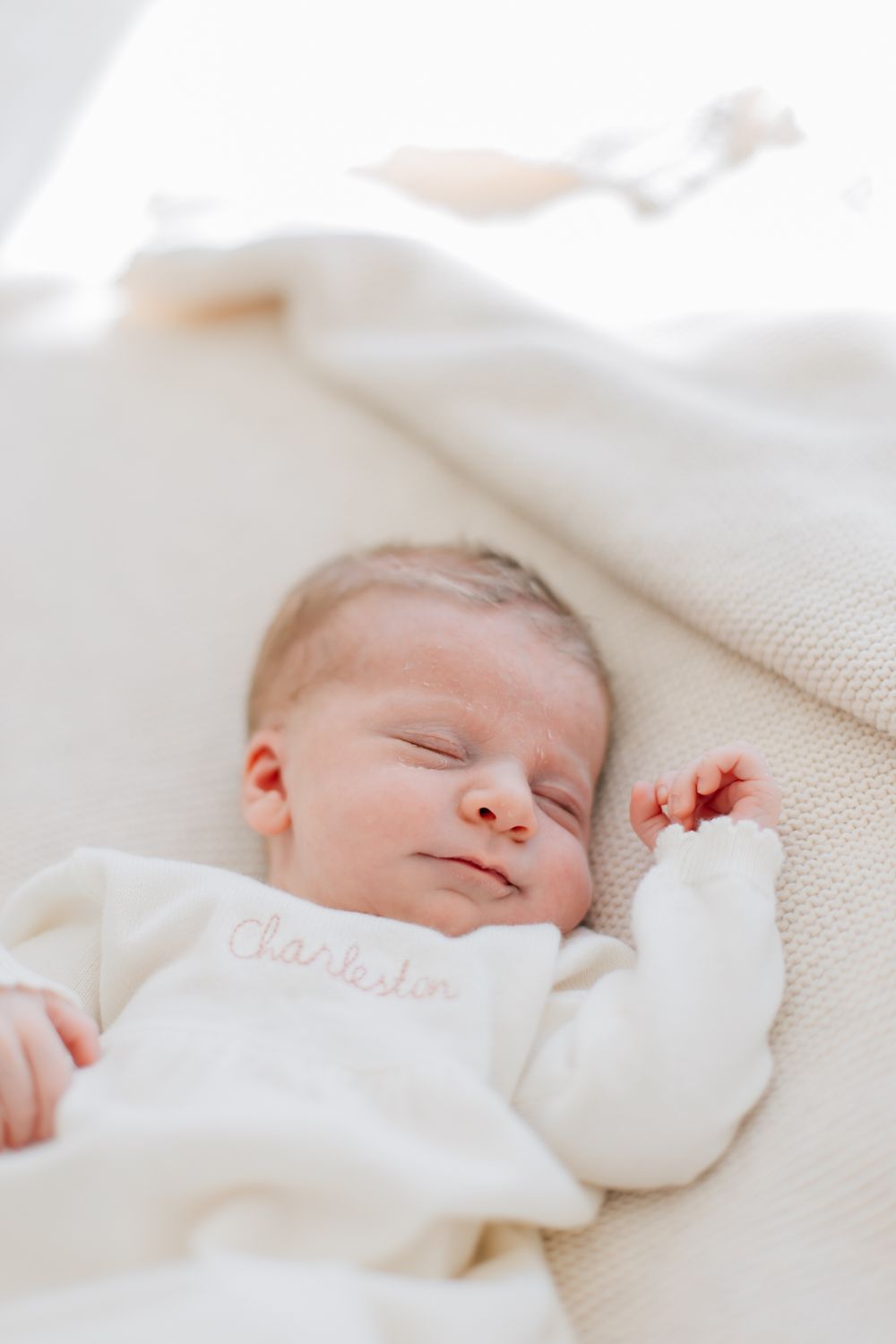 A peaceful sleeping baby wearing a white sweater lies on soft cream-colored bedding.