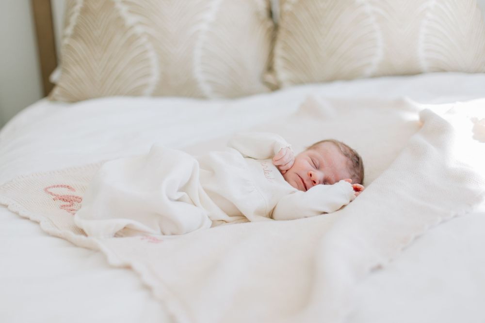 A sleeping newborn baby wrapped in white blankets lies peacefully on soft white bedding.