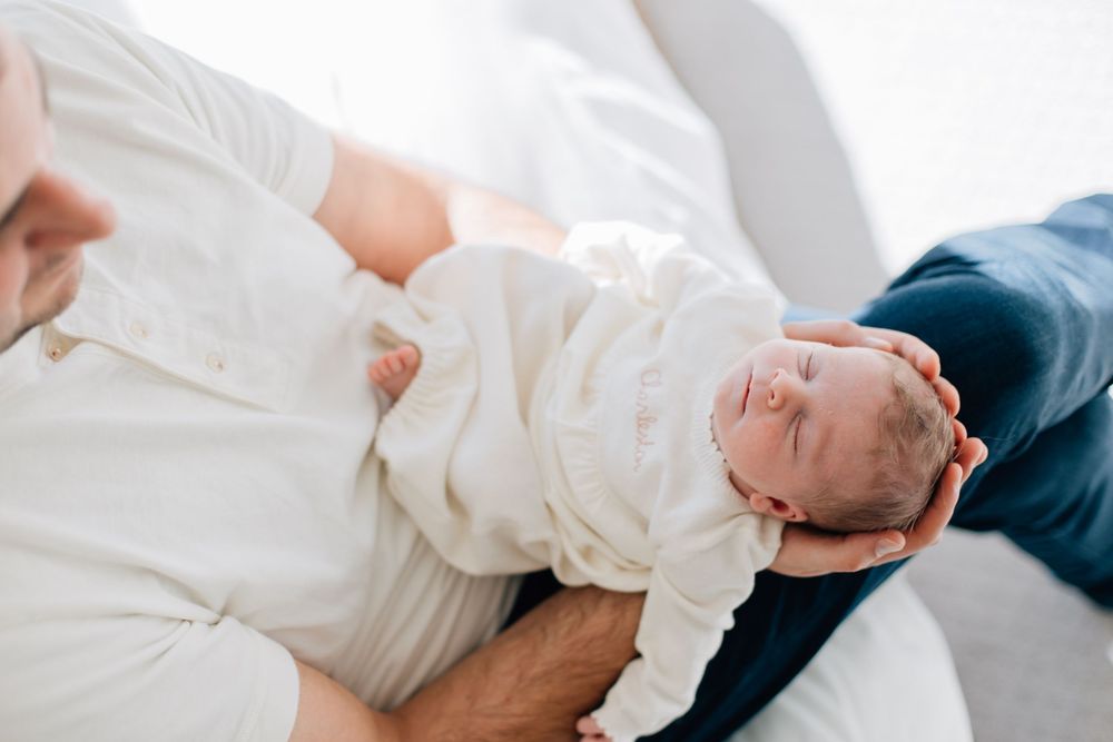 A sleeping newborn baby swaddled in white cloth rests on soft bedding.
