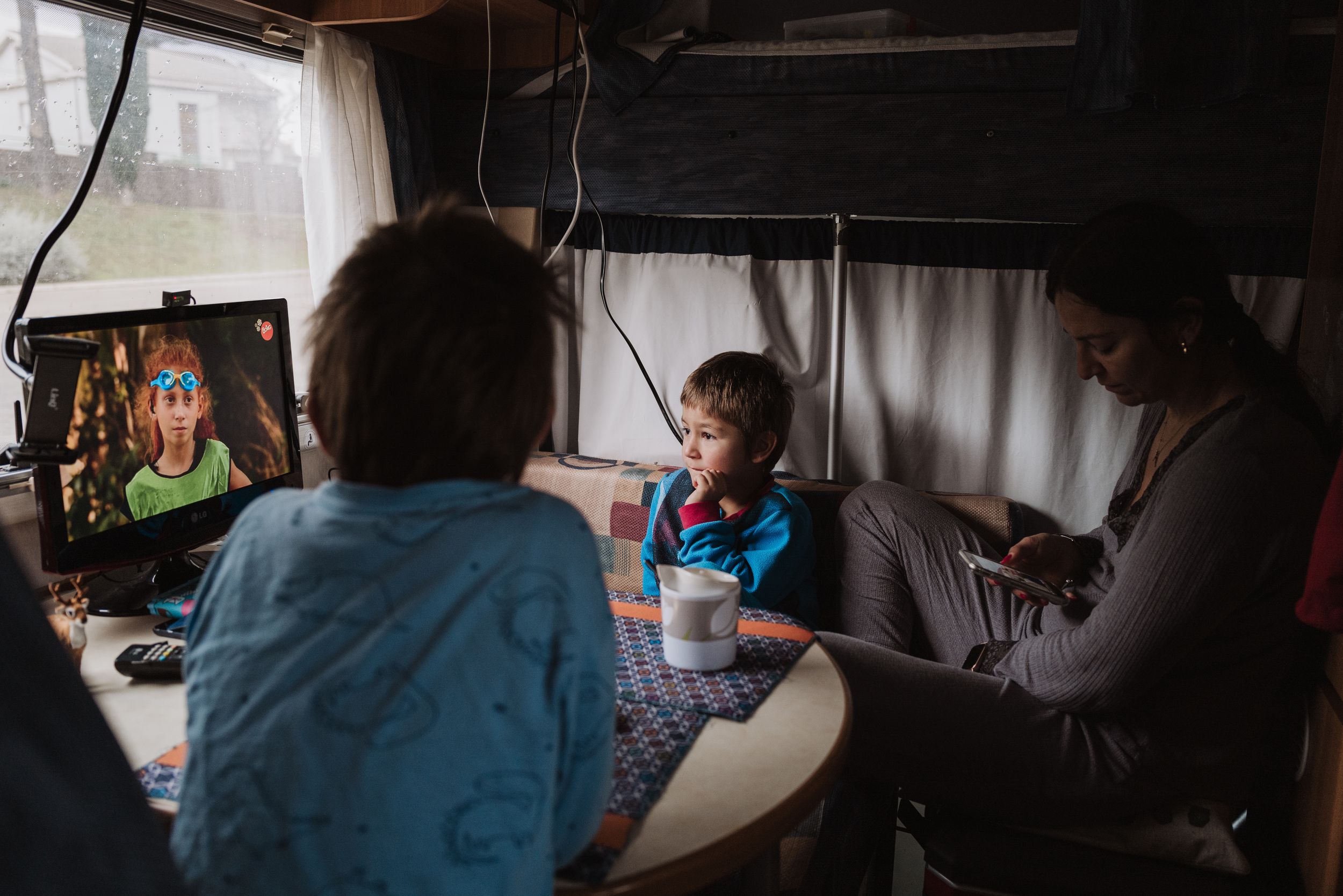 People gathering in a recreational vehicle interior with cozy lighting while using electronic devices for entertainment.