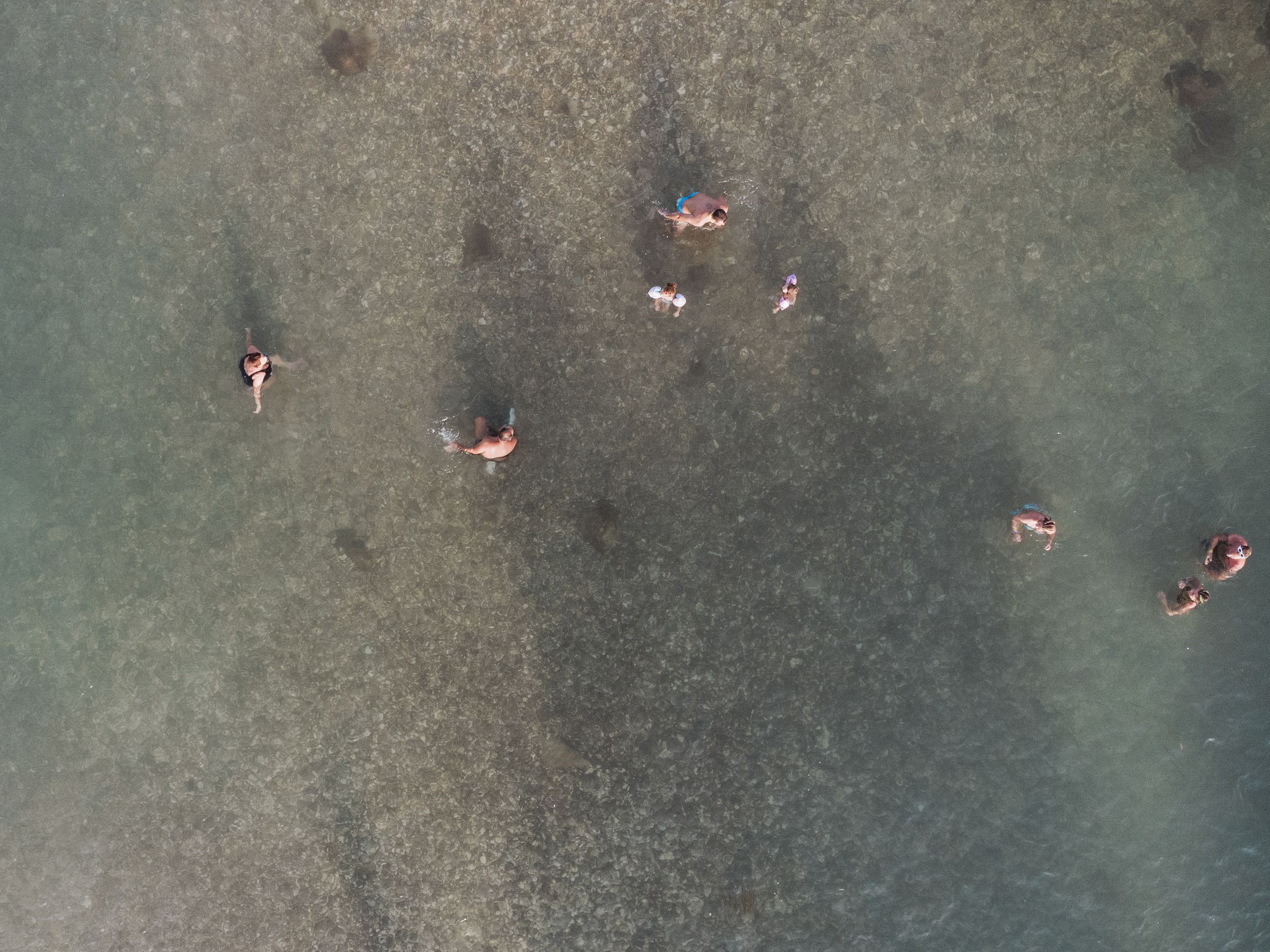 Aerial view of multiple swimmers scattered in dark blue-green water seen from directly above.