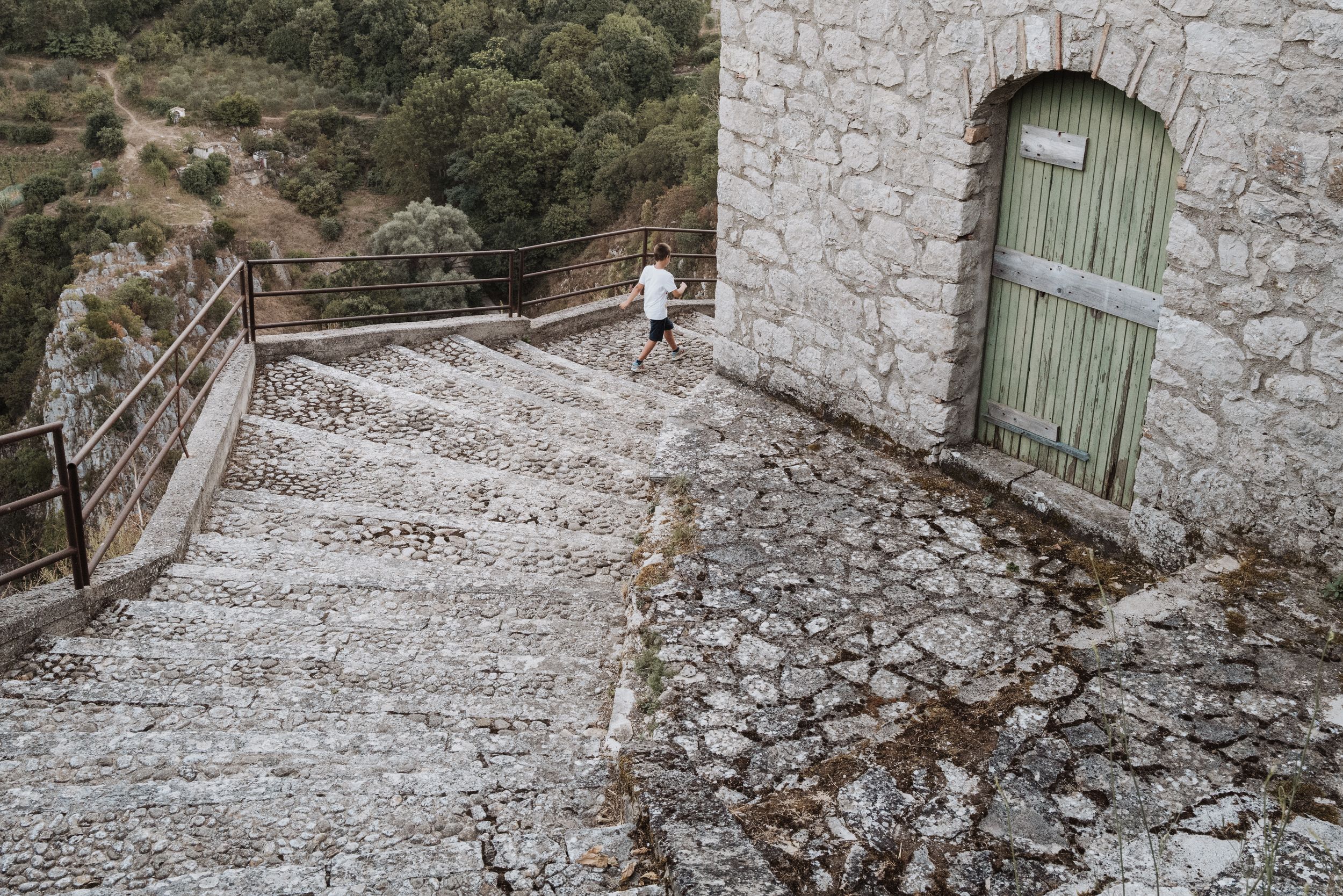 Stone stairway leading to a mint green door on a rustic building with mountain landscape in the background.