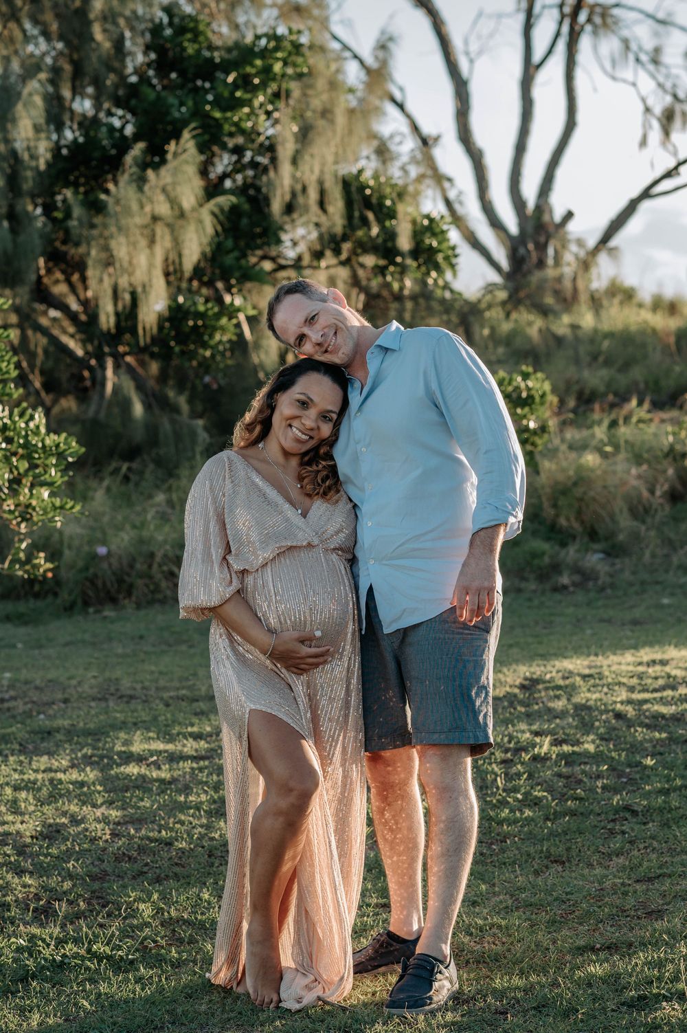 A couple stands together in a garden setting with Spanish moss hanging from trees in the background at sunset.