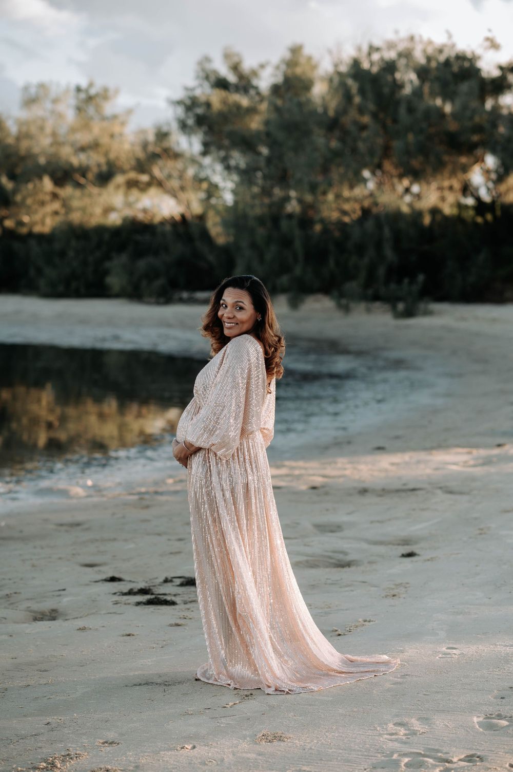 A sunset beach maternity photo featuring a sparkly blush gown and natural coastal backdrop.