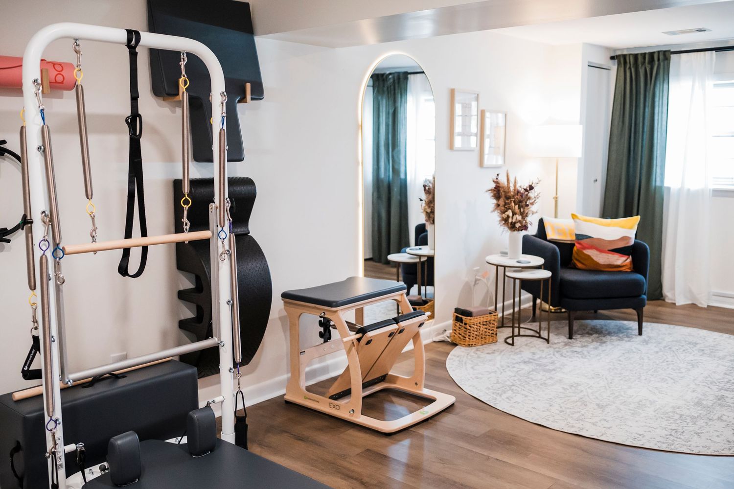 Modern home gym area setup with weight machine, pilates reformer, and comfortable reading nook featuring teal curtains.