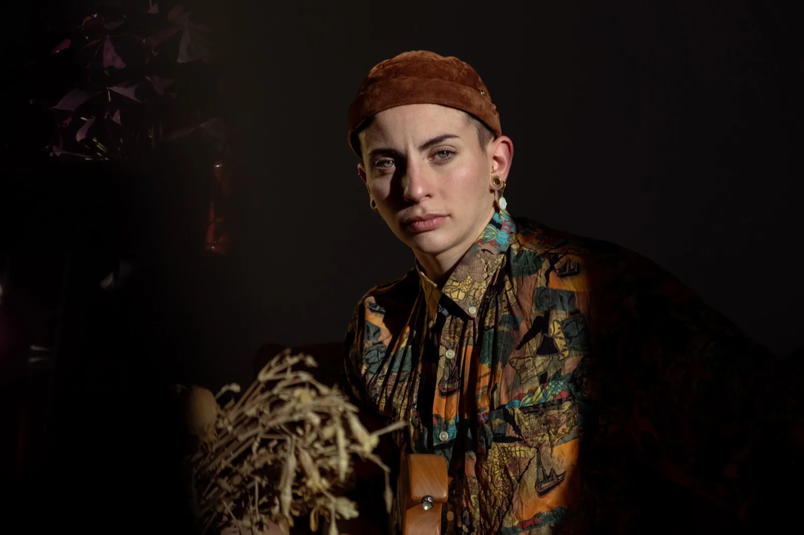 Portrait en clair-obscur d’une femme au regard intense, habillé d’une chemise à motifs floraux.