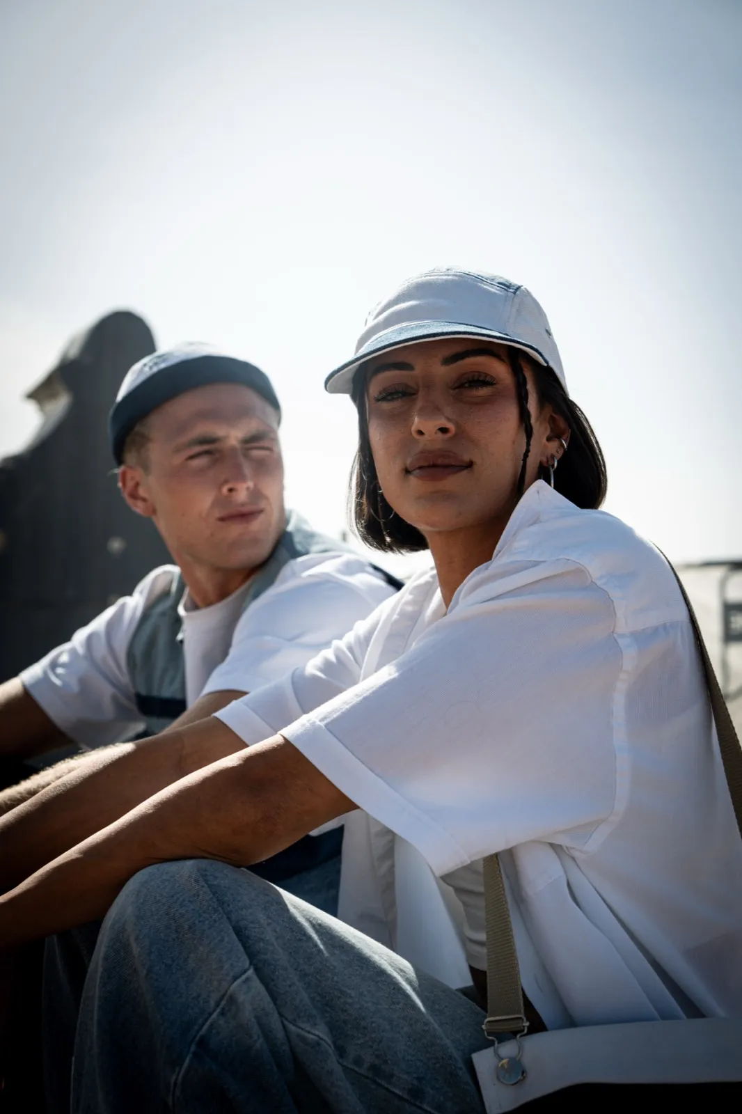 Deux jeunes personnes assises au soleil, regardant en direction de la caméra, ambiance décontractée.