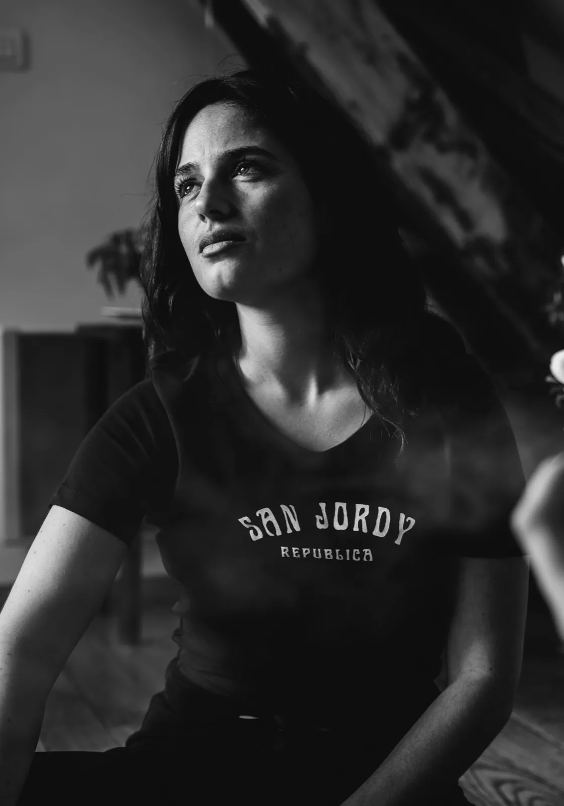 Portrait en noir et blanc d’une femme regardant vers le haut, portant un t-shirt “San Jordy”.
