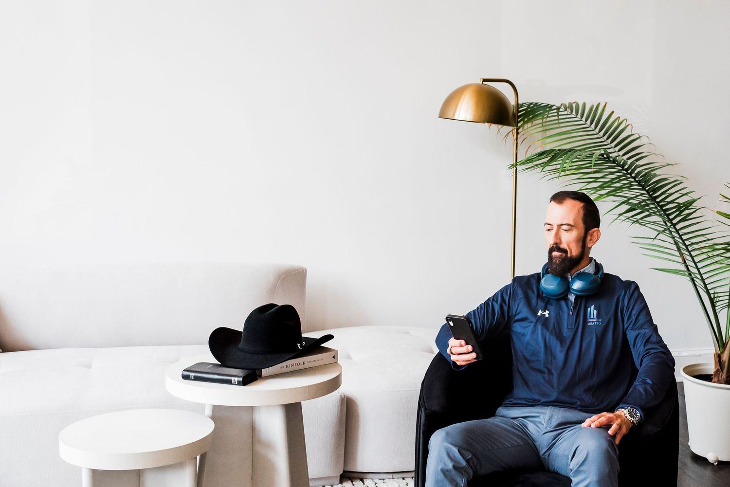 Casual scene with someone relaxing on a chair near a potted palm plant and brass floor lamp in minimalist room setting.