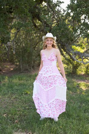 Twirling in a pink floral maxi dress and white cowboy hat in a grassy field.
