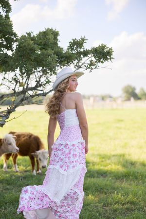 A scenic country portrait in a flowing dress with cows grazing in the background.