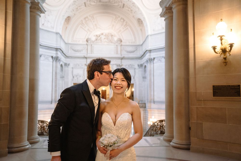 Romantic wedding moments unfold in a bright marble corridor with classical architectural elements.